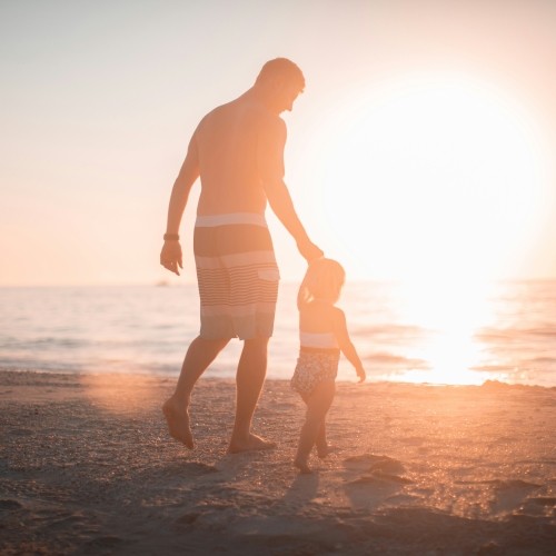 Father and son walking along the beach at sun set